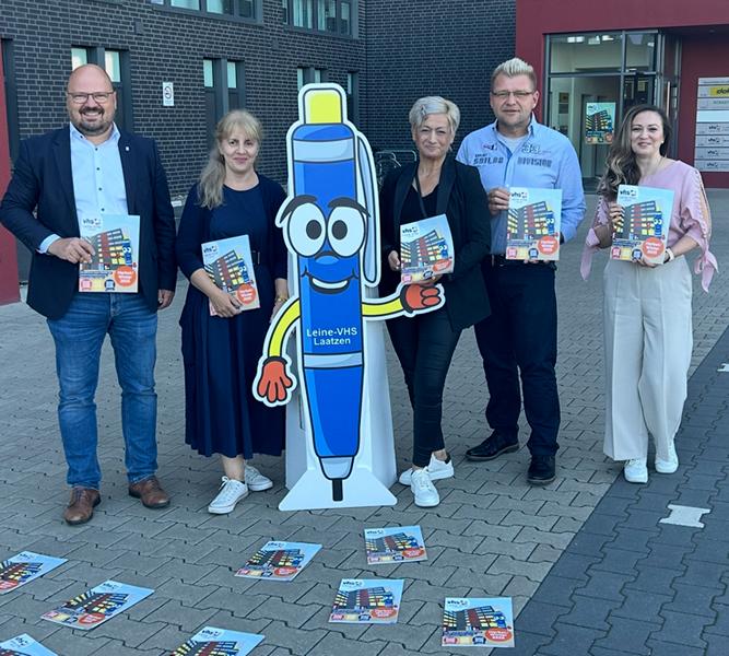 5 Personen inklusive Kai Eggert posieren mit den neuen Programmheften vor dem VHS Gebäude.