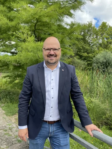 Bürgermeister Kai Eggert lächelt in die Kamera. Ersteht im Sommer vor einer grünen Wiese an einem Geländer