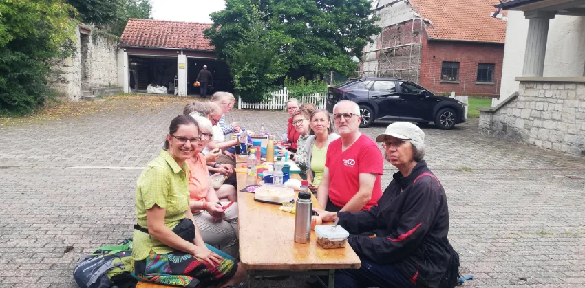 eine Gruppe von Menschen sitzt an einem Bierzelttisch mit Speisen und Getränken mitten auf einem Hofplatz